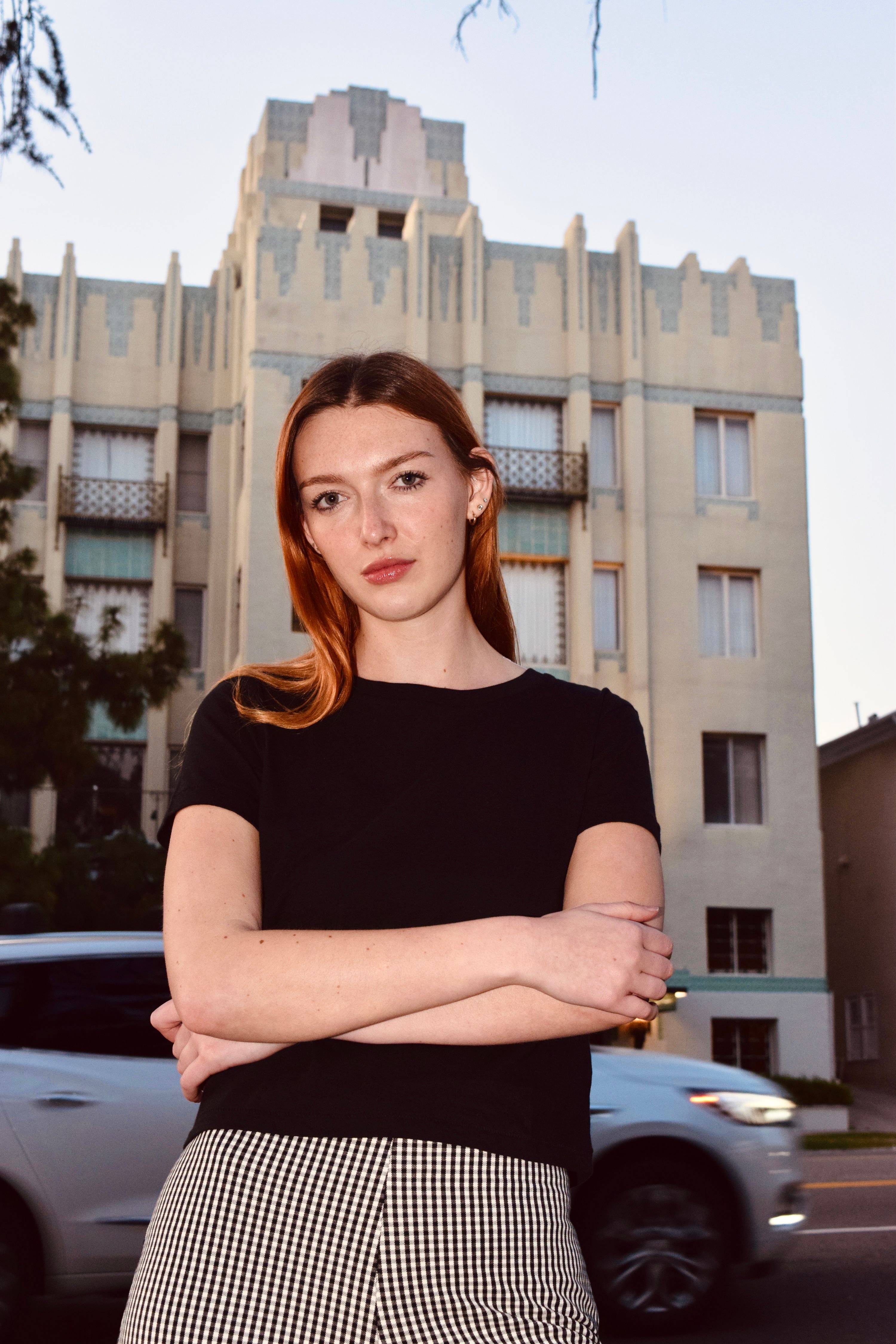 Confident young woman stands in front of an Art Deco building in Los Angeles.