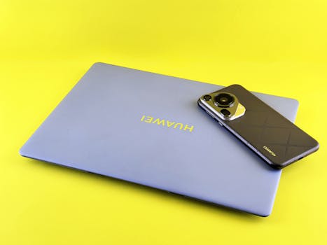 Modern laptop and smartphone displayed on a bright yellow background, showcasing technology elegance.
