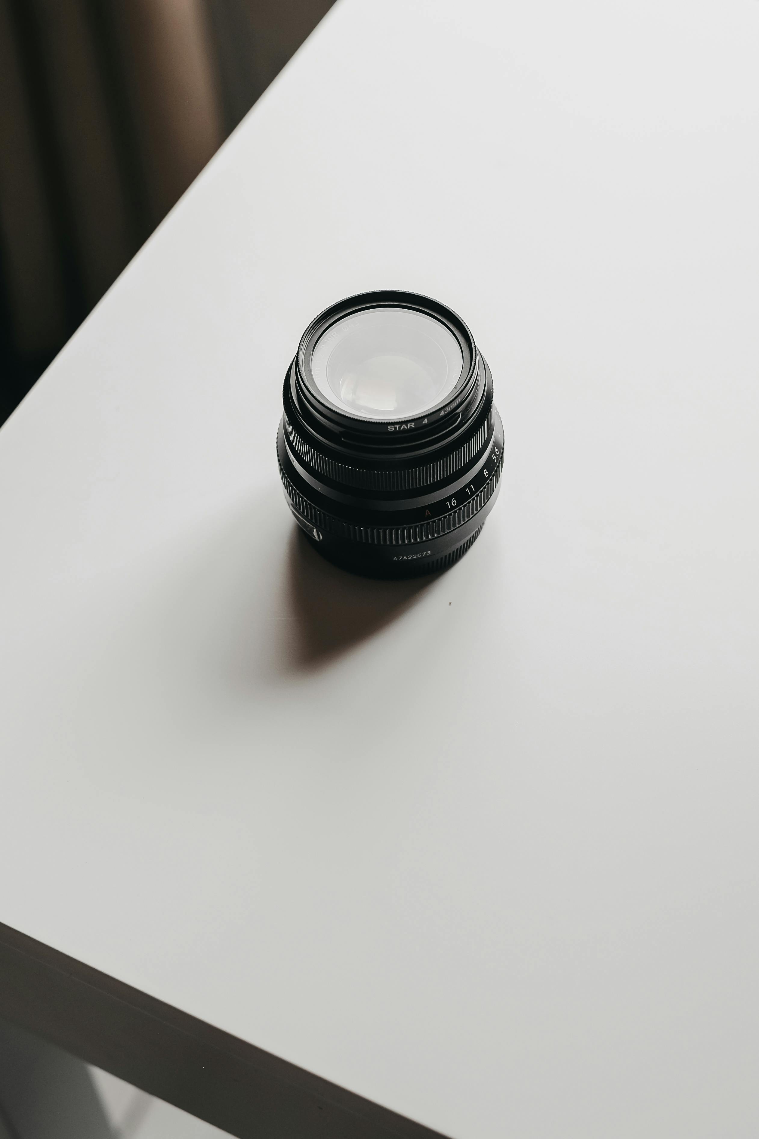 Gratis Un singolo obiettivo fotografico posizionato su un tavolo bianco che mette in mostra uno stile fotografico minimalista. Foto a disposizione