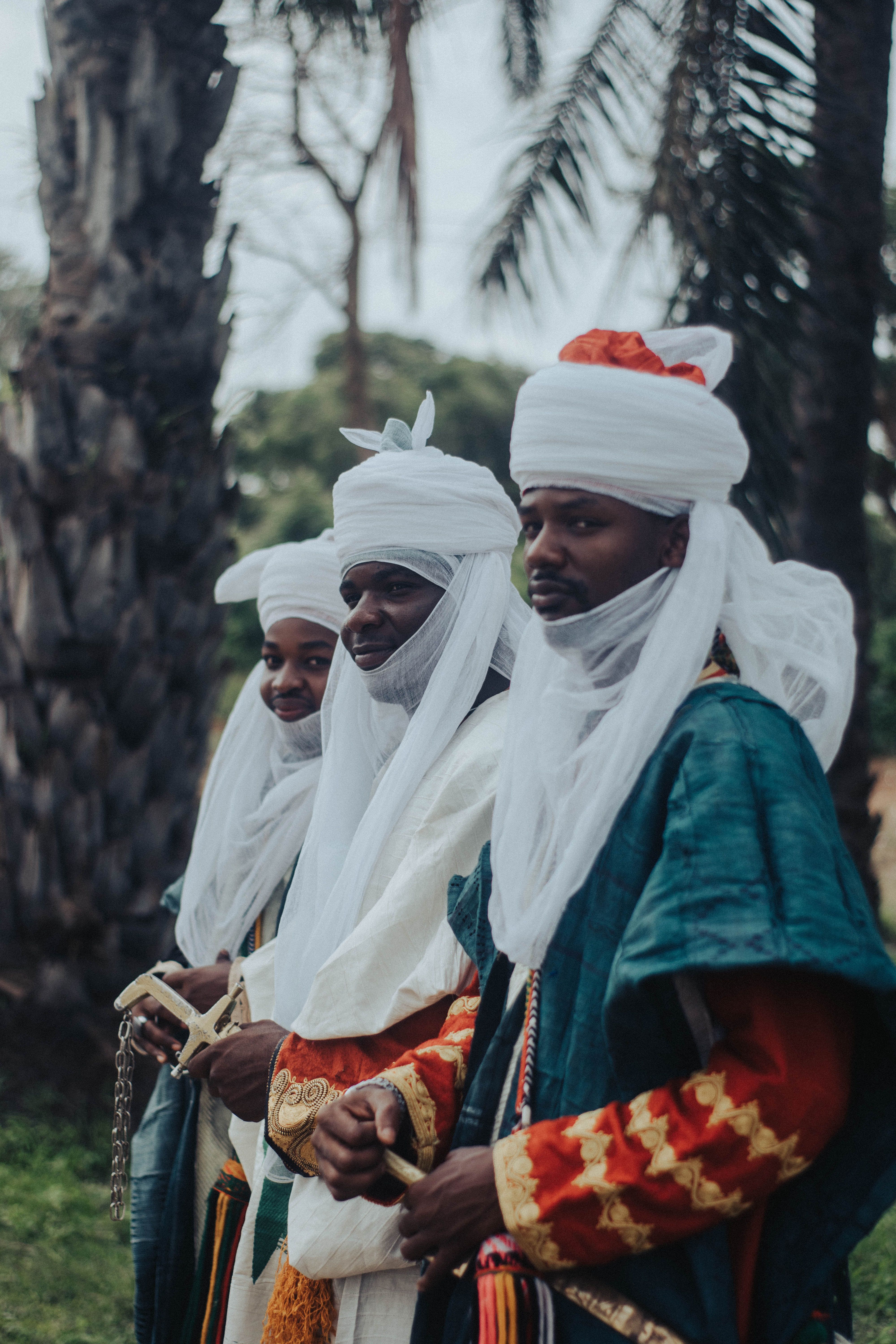 Gratis Tre uomini in vivaci abiti tradizionali africani e con copricapi, in piedi all'aperto. Foto a disposizione