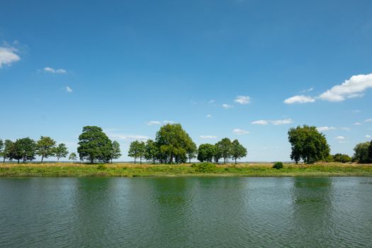 Scenic view of a tree-lined riverbank with a sunny blue sky in France, capturing the serenity of summer.