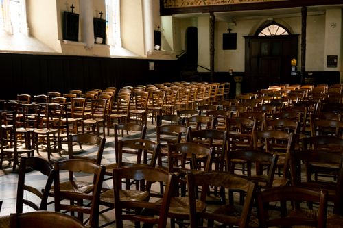 Free A serene church interior in France featuring rows of wooden chairs illuminated by warm sunlight through the windows. Stock Photo