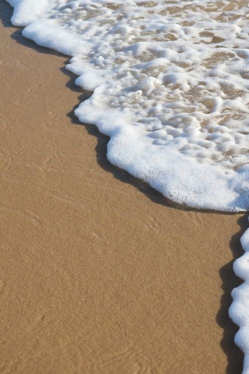 Free Close-up of foamy waves lapping onto Lacanau's sandy beach, capturing summer's serene essence. Stock Photo