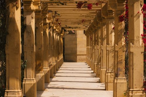 Free Sunlit stone pathway with elegant columns and red flowers in a serene setting. Stock Photo