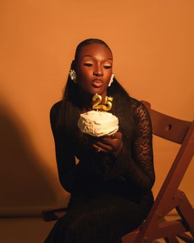 Stylish woman in black dress holding a 25th birthday cake with golden candles.