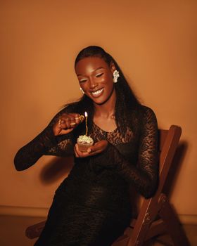 Gorgeous woman in a black dress lighting a cupcake candle with a joyful smile.
