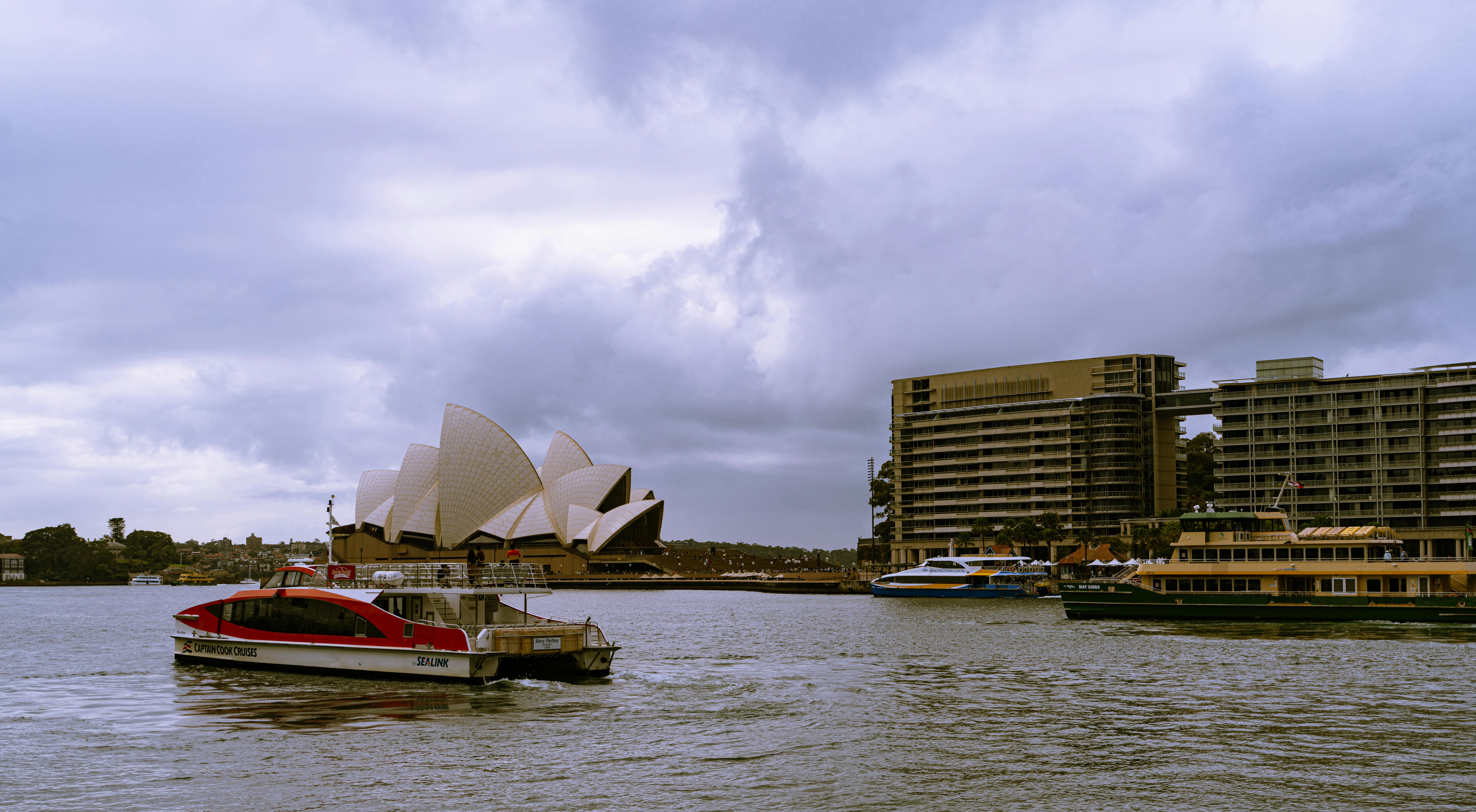 Scenic view of Sydney Opera House and bustling harbor in cloudy weather, New South Wales, Australia.