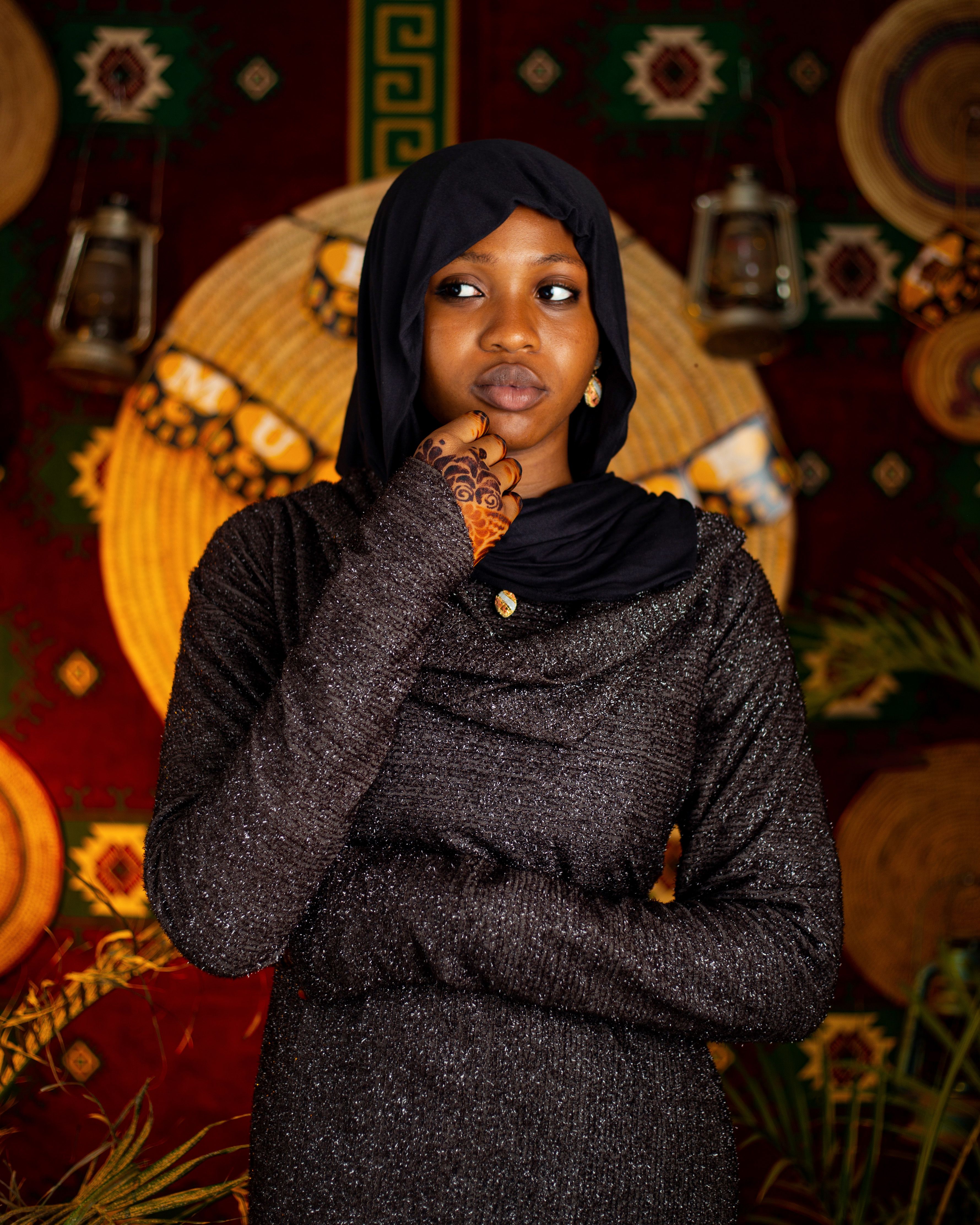 Stylish woman in black hijab with henna design on hand, vibrant traditional decor background.