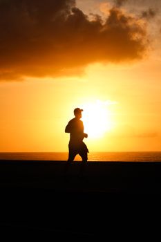 A jogger silhouetted against a vibrant sunset at the beach in Salvador, Brazil.