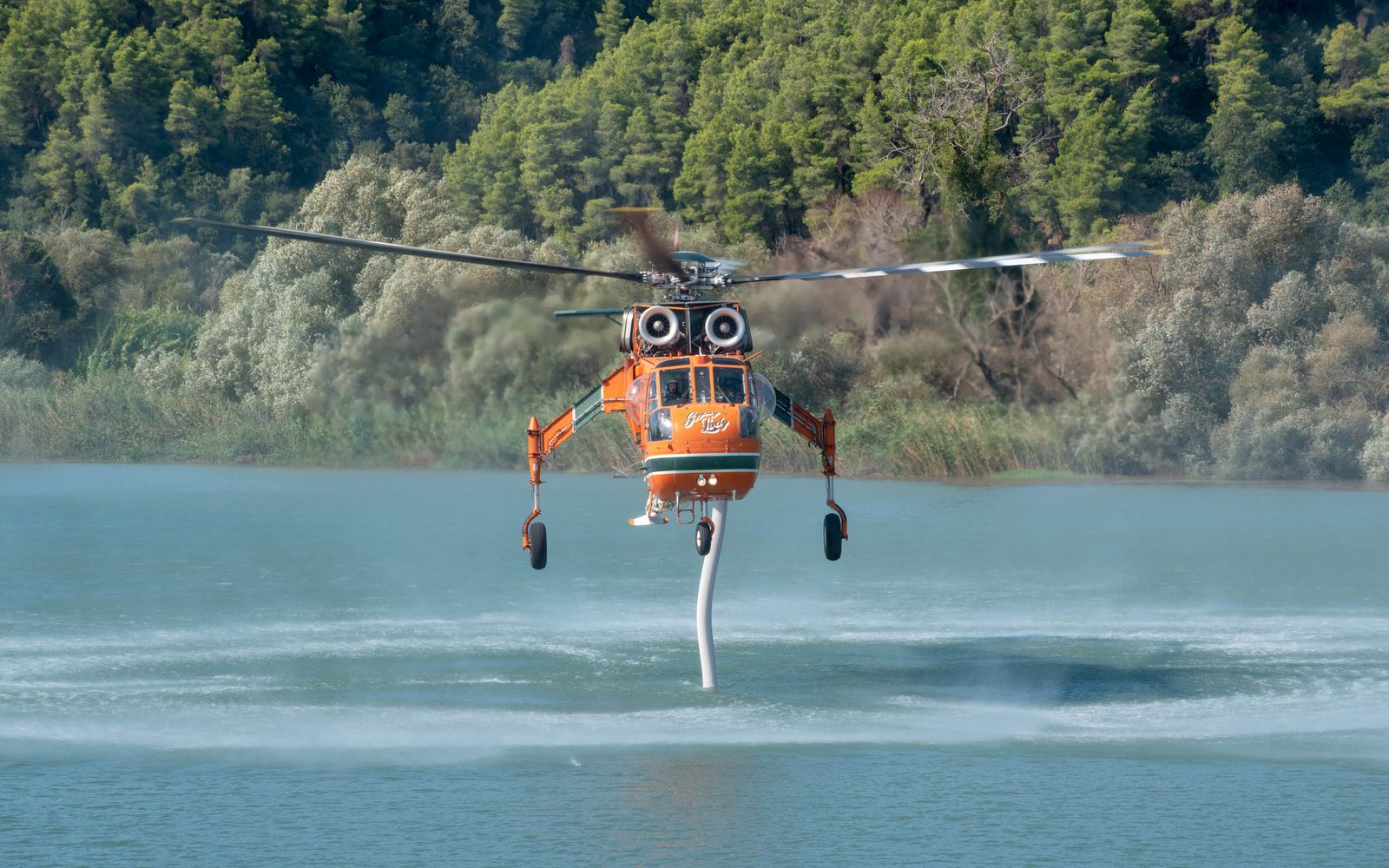 An aerial firefighting helicopter drawing water from a river in Greece during wildfire operations