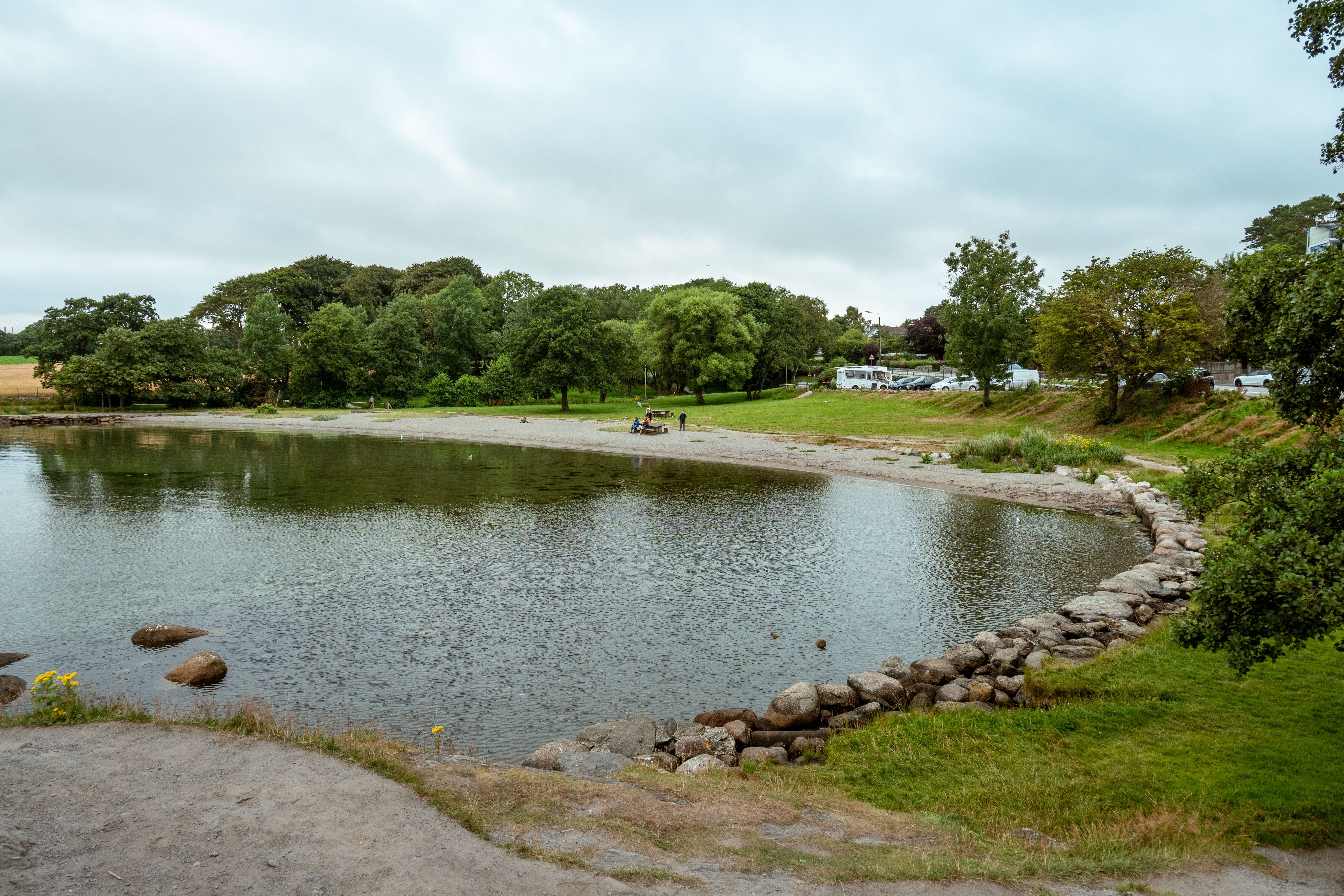 Tranquil beach scene at Lindesnes, Agder, Norway with lush greenery and calm waters.