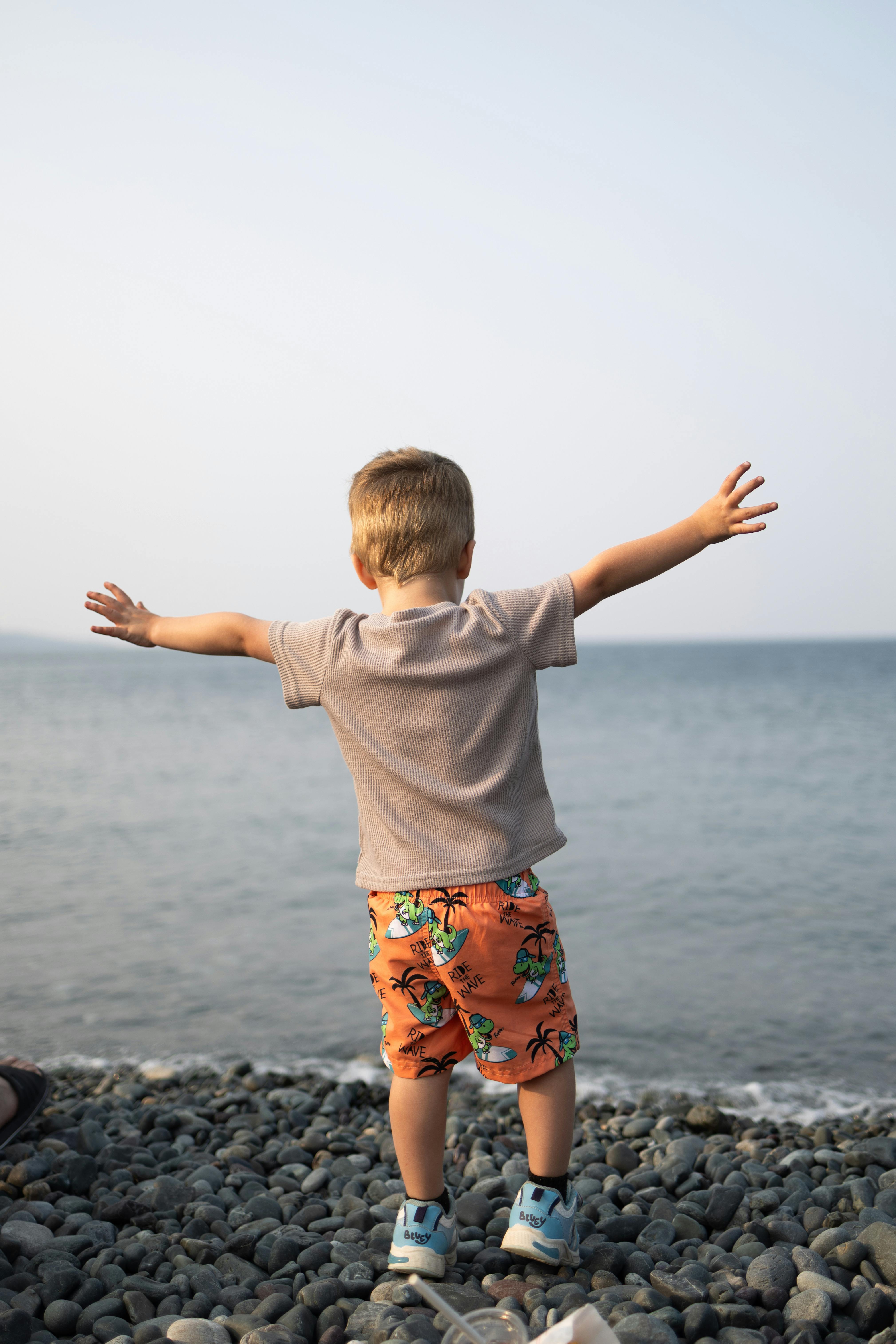 Young child with open arms embracing the sea view at a rocky beach.