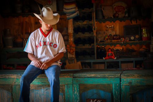 Free A man in a cowboy hat and 'México' shirt sitting in a rustic, decorative setting. Stock Photo