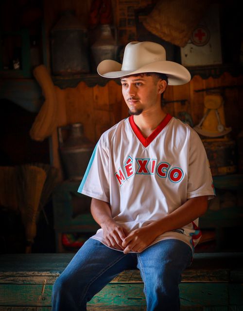 Free A young man sits indoors wearing a cowboy hat and México jersey, creating a cultural blend. Stock Photo