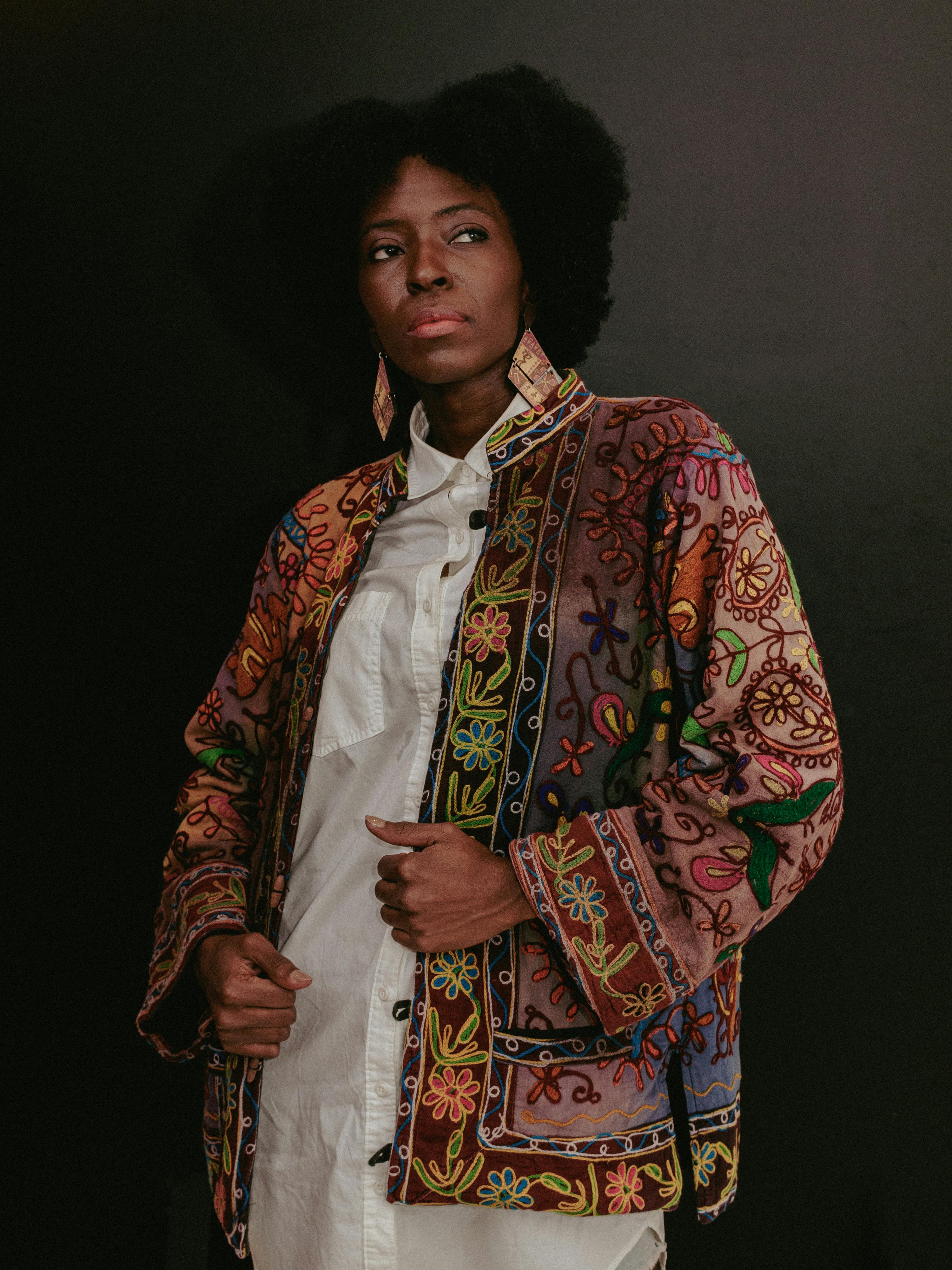 Elegant portrait of a woman wearing a vibrant embroidered jacket against a dark backdrop.