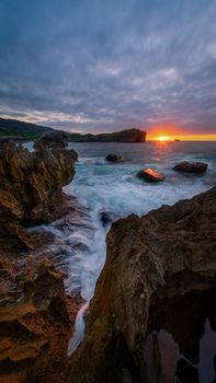 Stunning view of a rocky coastline with waves crashing at sunset under a dramatic sky.