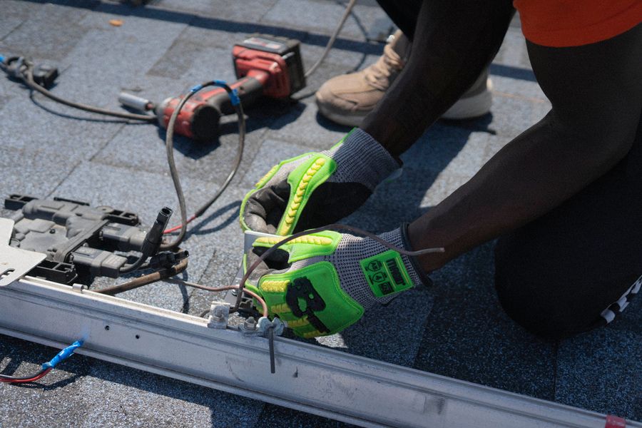 Gloved hands connecting wiring on a mounting rail on a roof