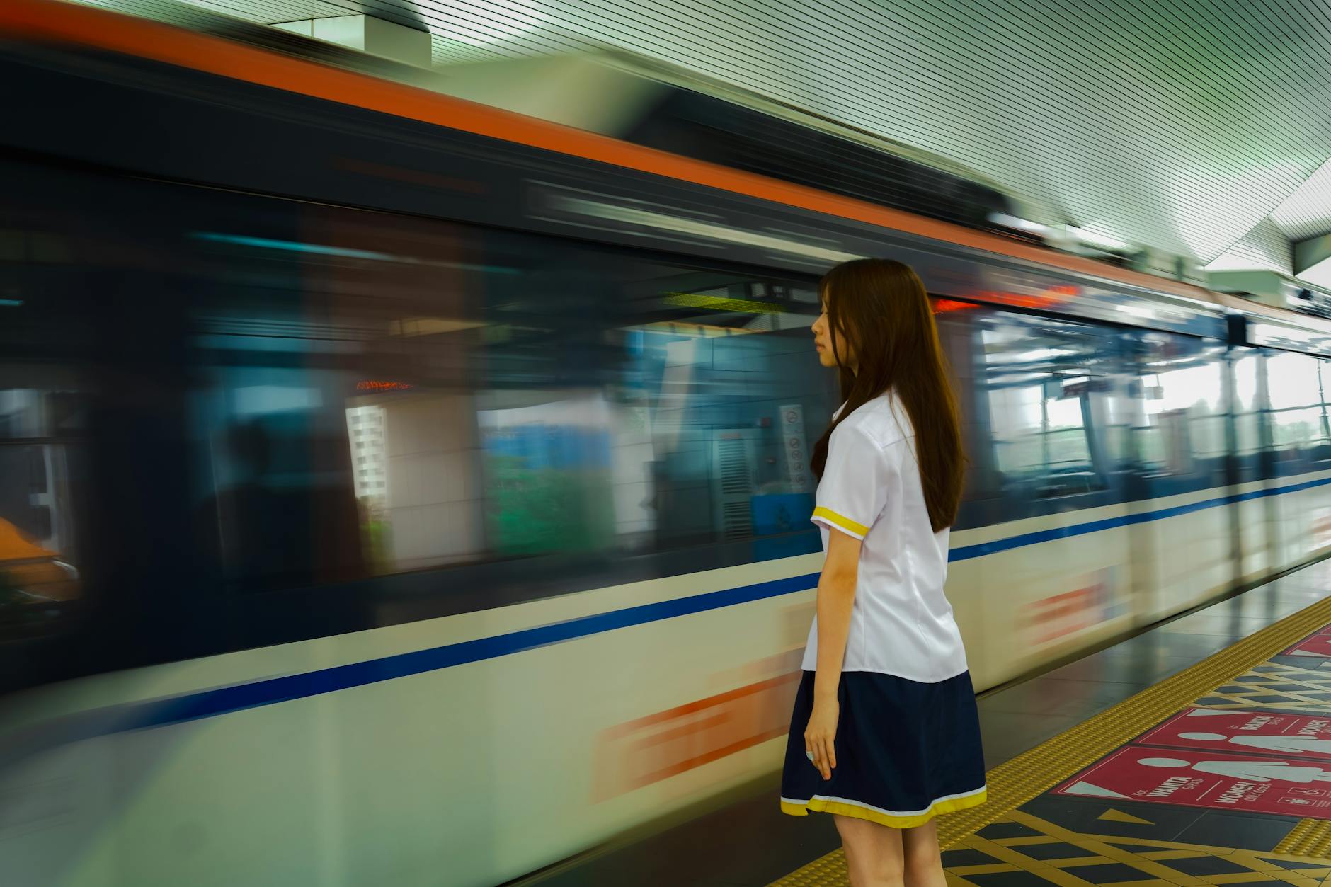 A young woman stands at a train station as a fast-moving train passes by.