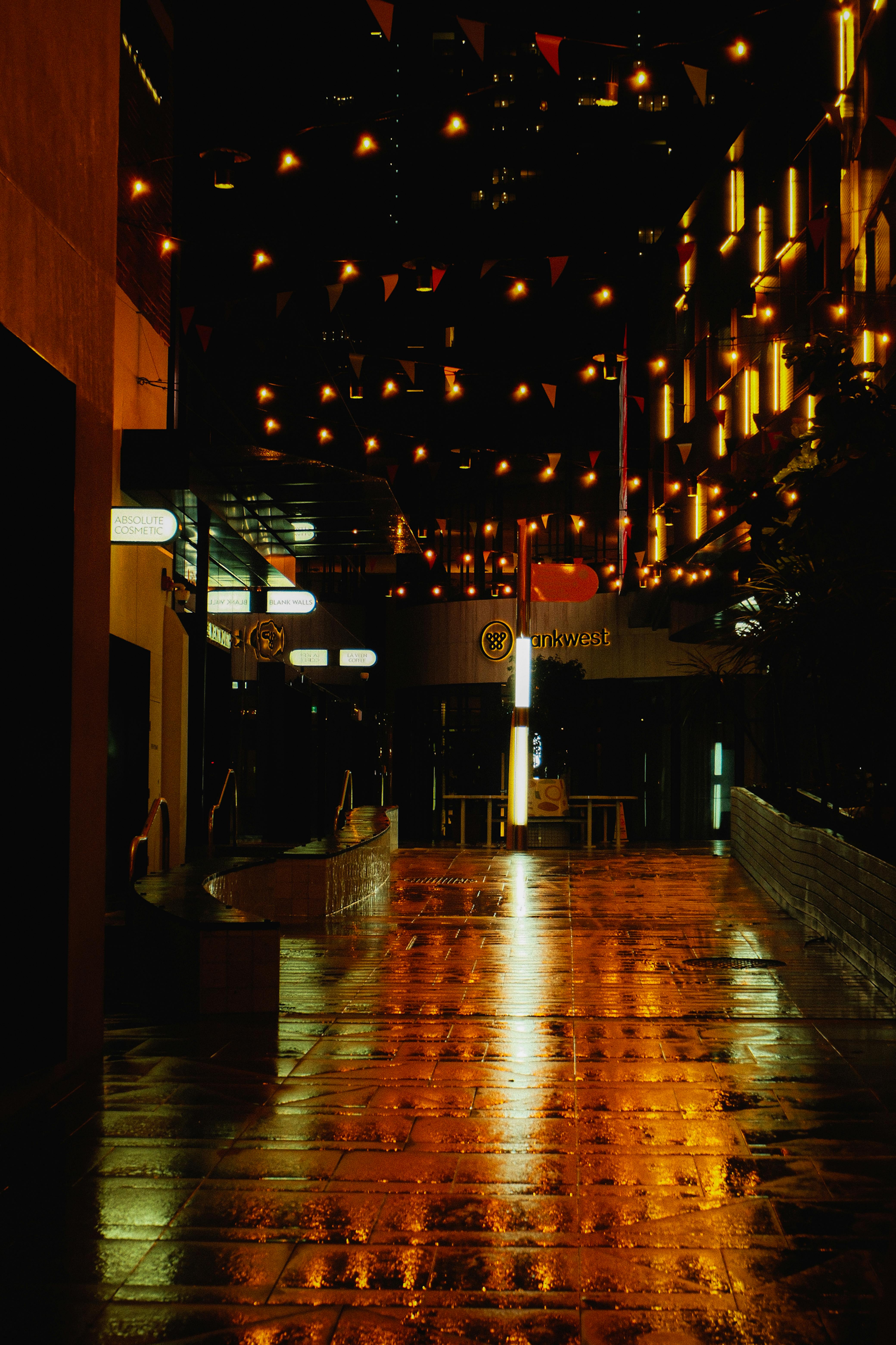 Безкоштовне Нічна міська сцена з сяючими вогнями, що відбиваються на мокрій вулиці, створюючи похмуру атмосферу. стокове фото