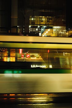Blurred train passing at night in a cityscape with illuminated buildings and reflections.