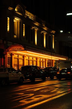 A beautifully lit historic building with parked cars captured at night, showcasing urban architecture.