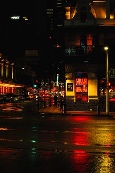 Vibrant city street at night with neon lights reflecting on wet pavement.