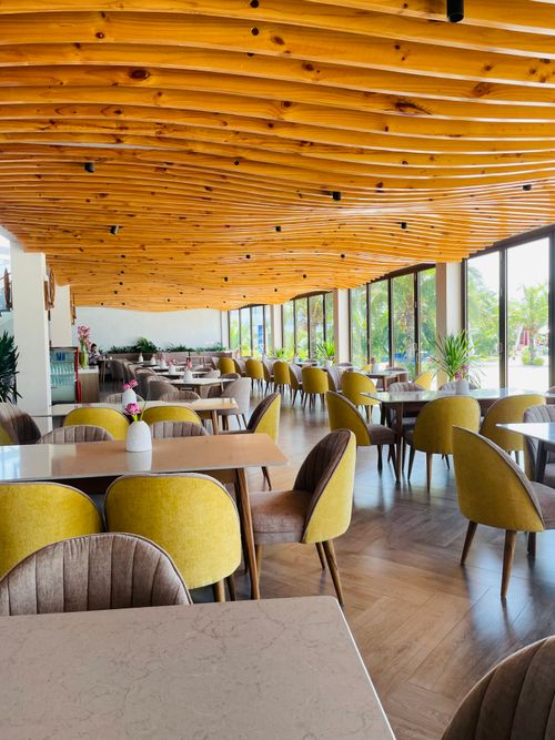 Free Bright restaurant interior featuring wavy wooden ceiling and large windows overlooking lush outdoor scenery. Stock Photo