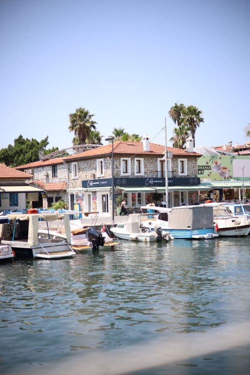 Free Scenic view of a cafe-lined waterfront with boats and palm trees under a clear blue sky. Stock Photo