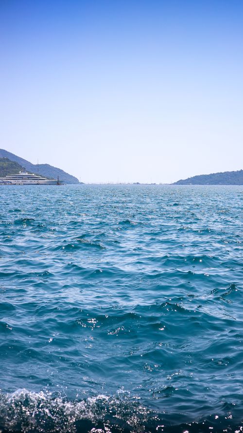 Free Peaceful ocean scene with gentle waves and distant hills under a clear blue sky. Stock Photo
