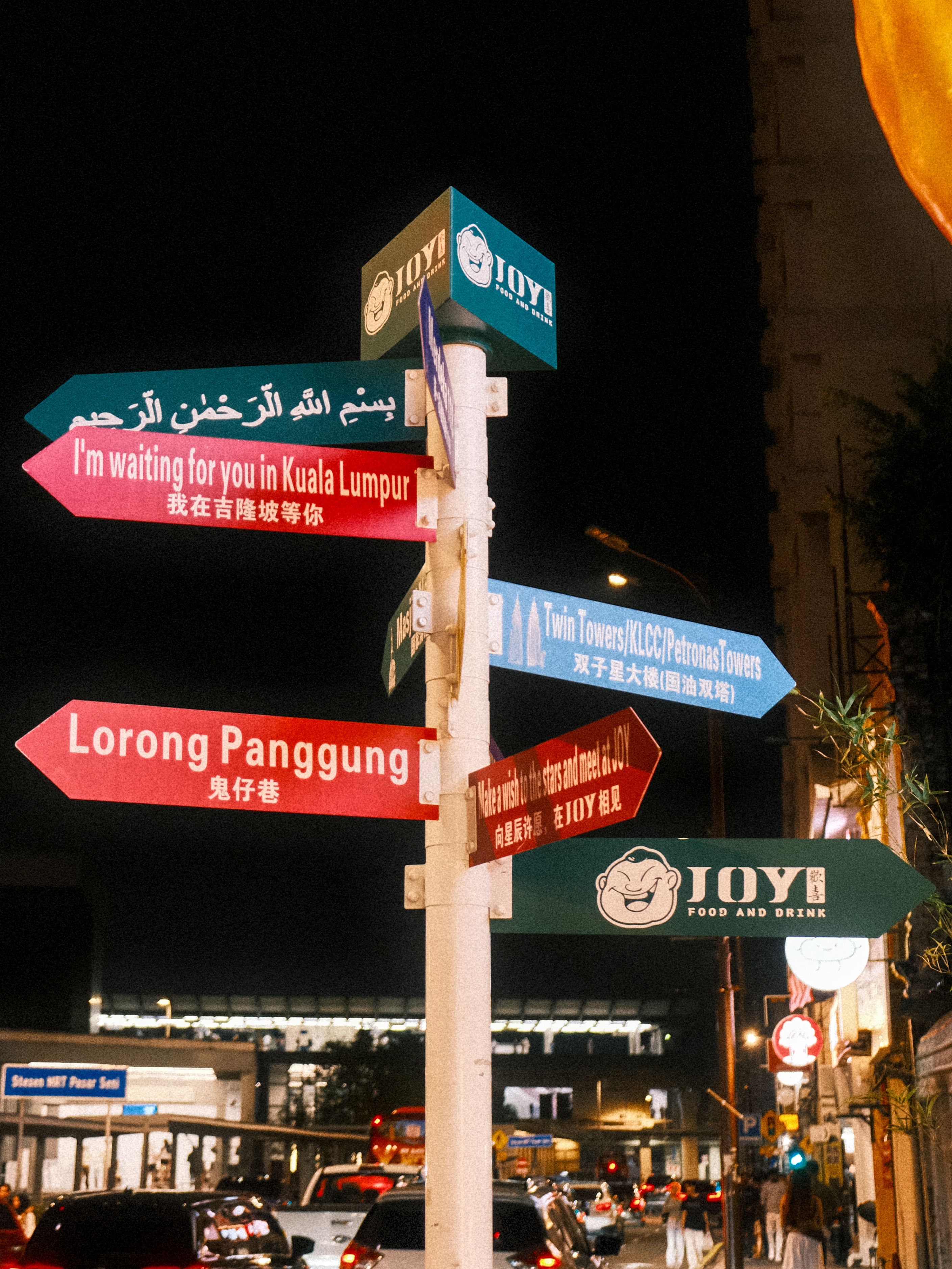 Colorful street signs in Kuala Lumpur at night, guiding to various locations.