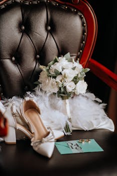 Elegant display of bridal accessories including white bouquet, shoes, and envelope on a chair.