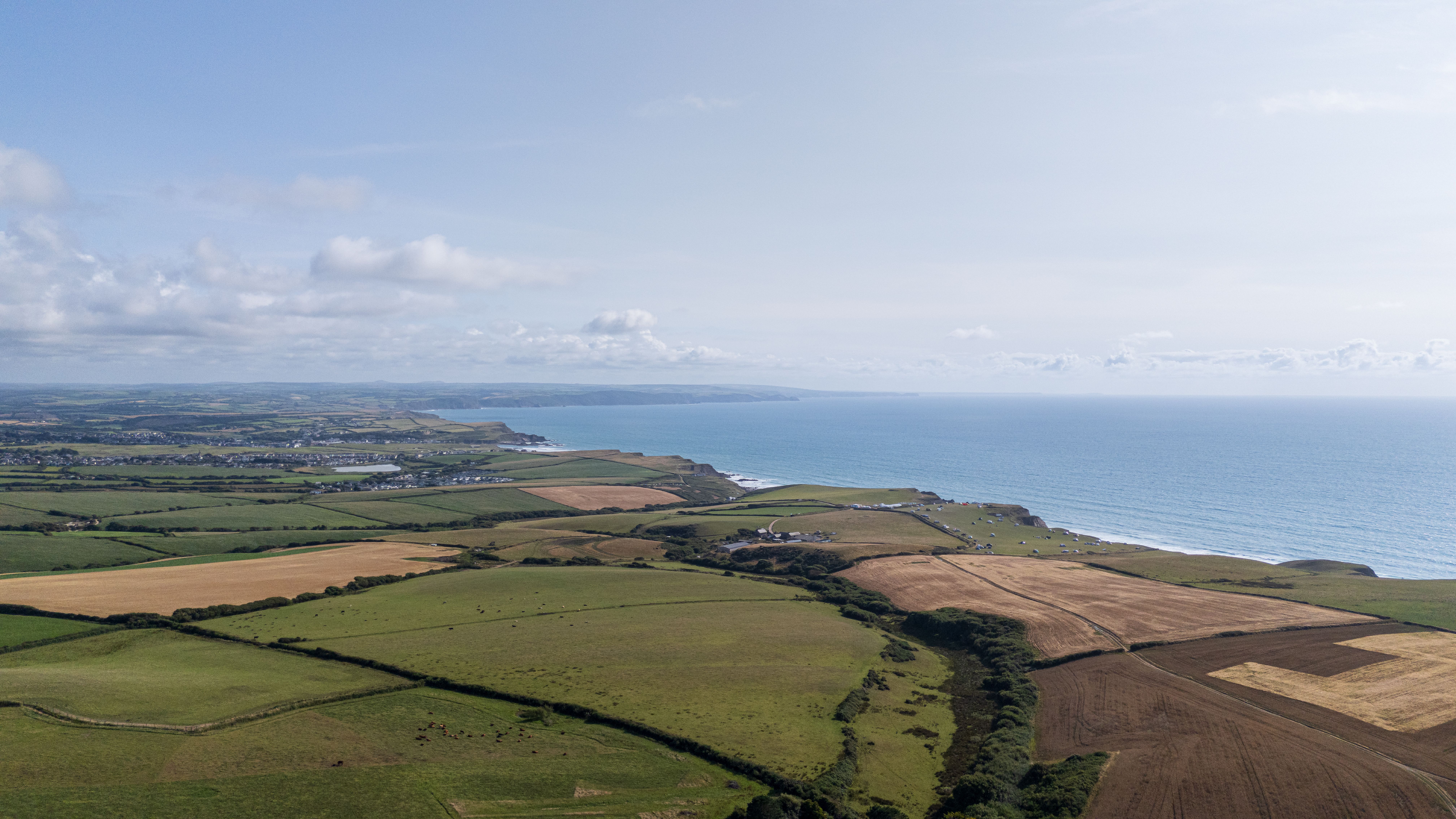 Stunning aerial view of the Cornish coast and patchwork farmlands under a bright sky.