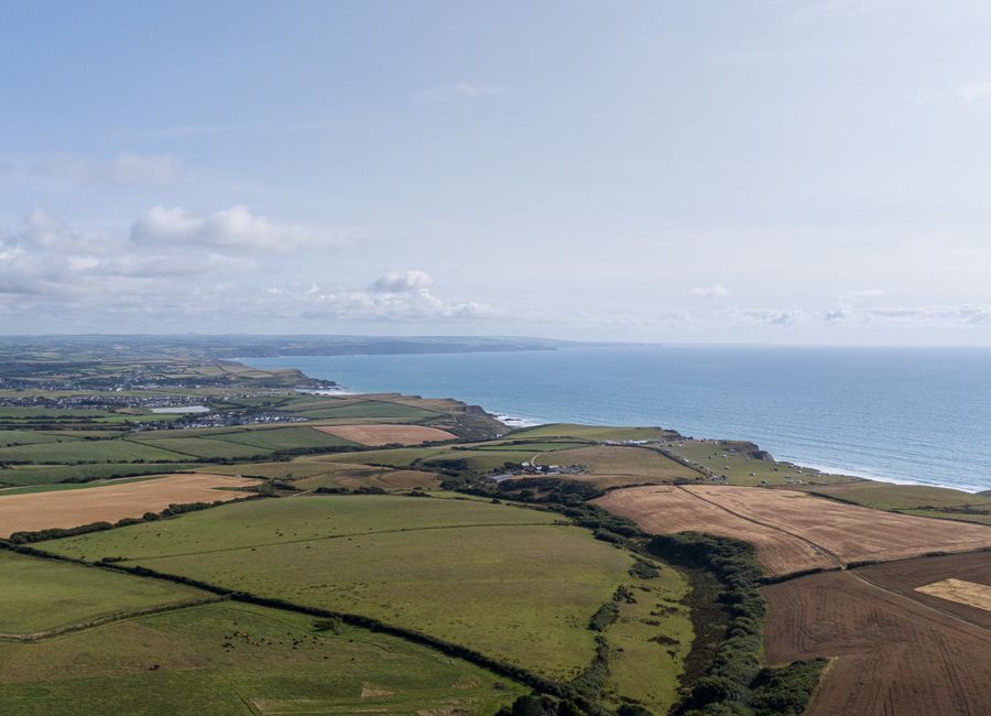 Stunning aerial view of the Cornish coast and patchwork farmlands under a bright sky.