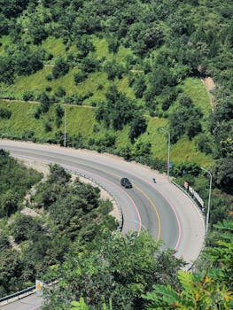 A winding road cuts through verdant hills, ideal for travel enthusiasts and nature lovers.