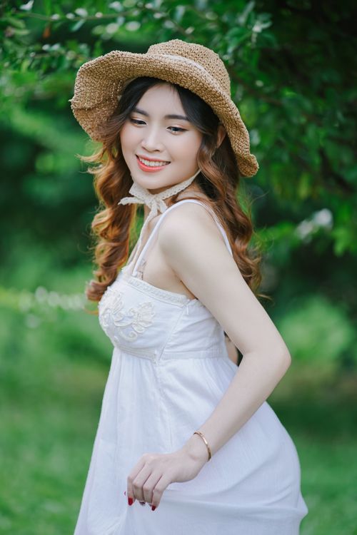 Free A young woman enjoys a sunny day in a white summer dress and straw hat in a lush green park. Stock Photo
