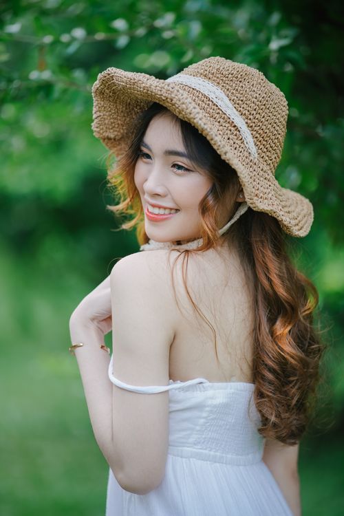Free Young woman wearing sun hat smiles in a garden setting, embodying summer elegance and warmth. Stock Photo