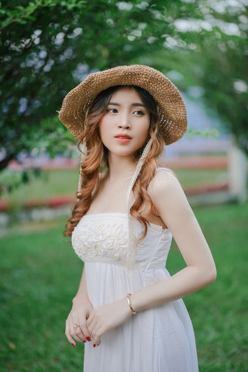 Free Charming young woman in a white dress and straw hat posing in a lush green garden. Stock Photo