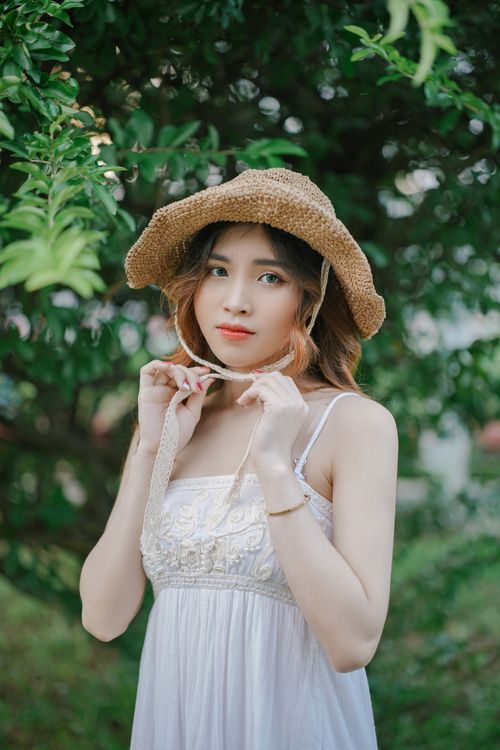 Free Elegant woman in a straw hat and white dress poses outdoors in summer greenery. Stock Photo