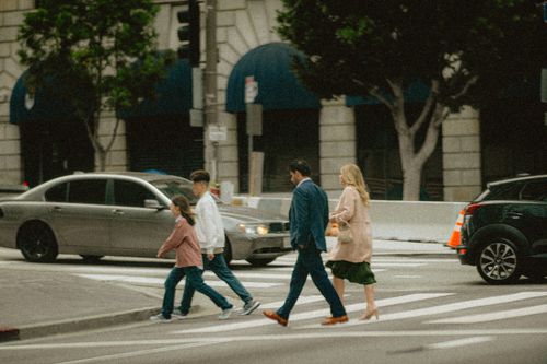 Free A family crosses a city street at a crosswalk surrounded by cars and buildings. Stock Photo