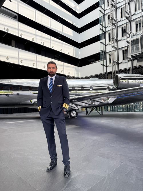 Free Confident pilot poses near private jet in modern building setting. Stock Photo