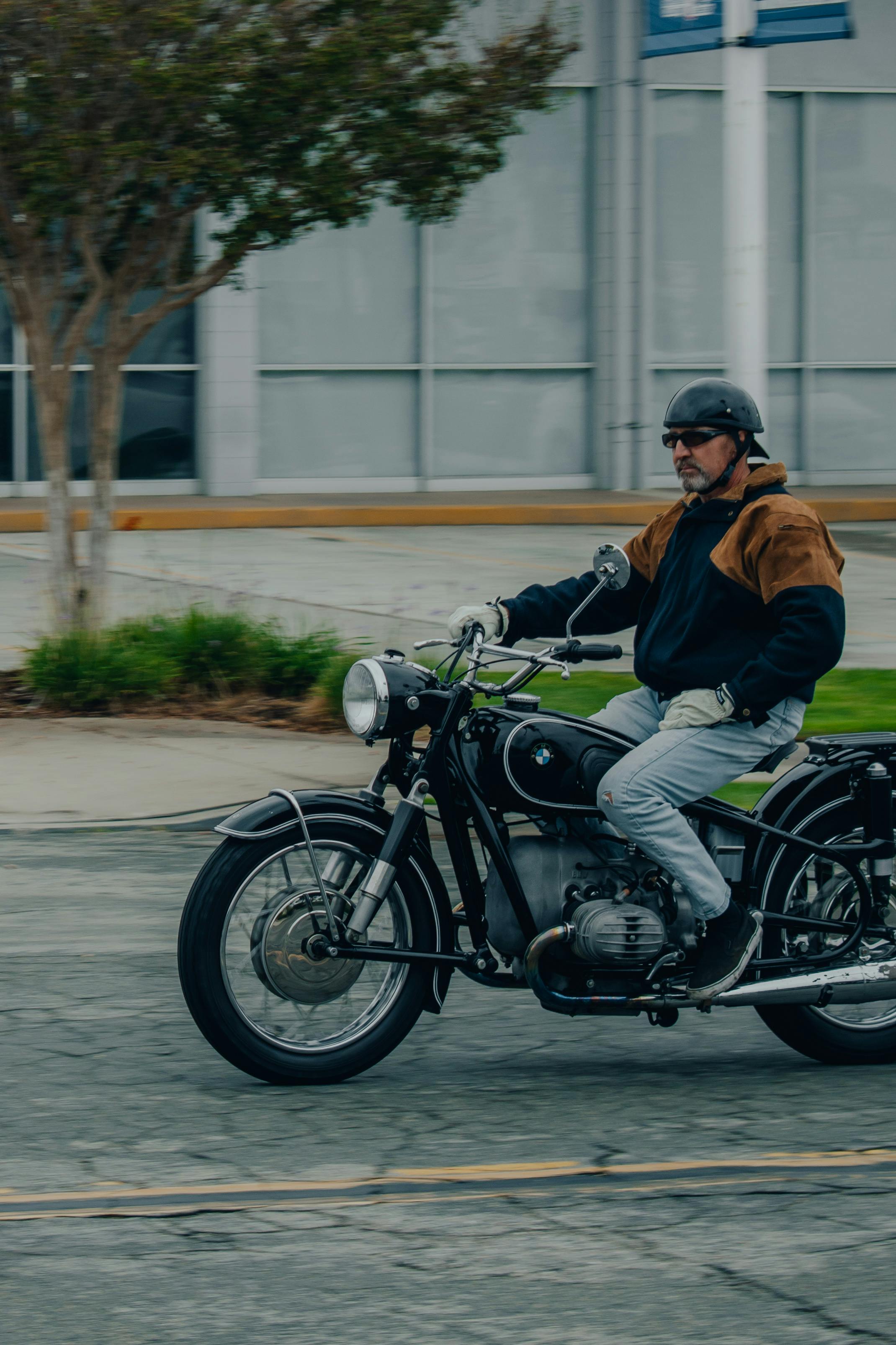 Free A man wearing a helmet rides an old motorcycle on a city street, showcasing vintage style and urban lifestyle. Stock Photo