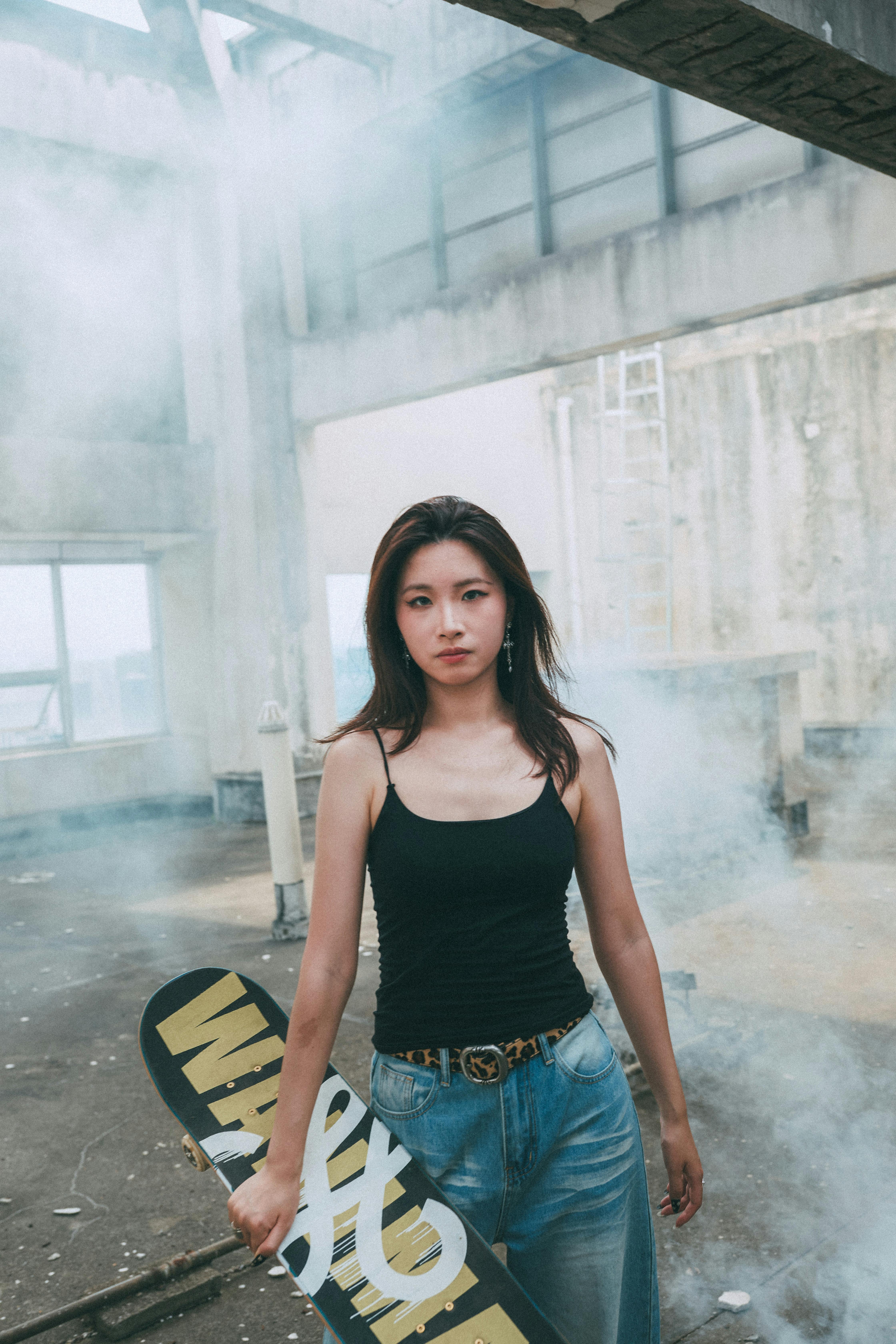 Young woman holding skateboard in urban setting, surrounded by mist.