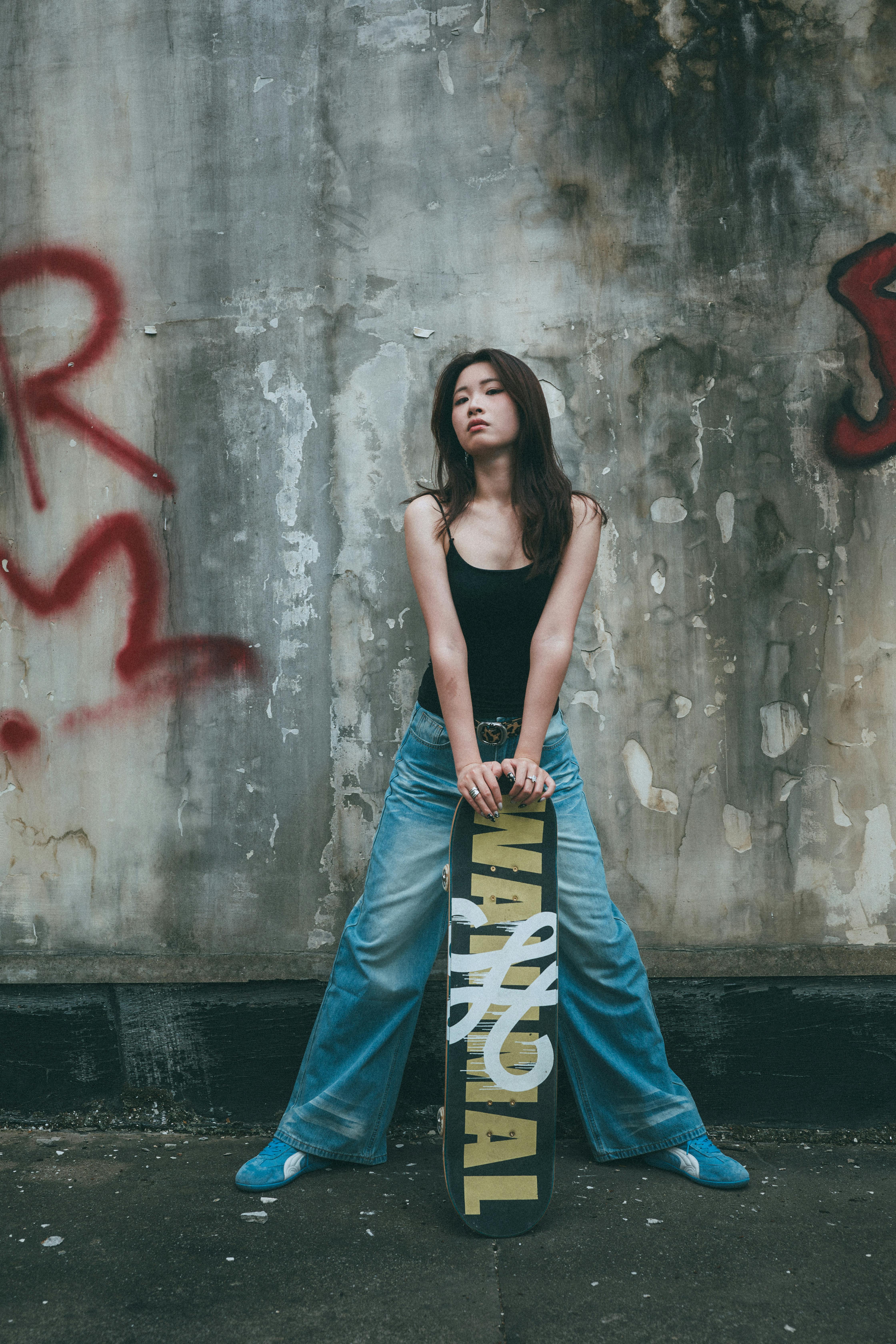 Confident young woman with skateboard in urban graffiti setting. Street style and attitude.