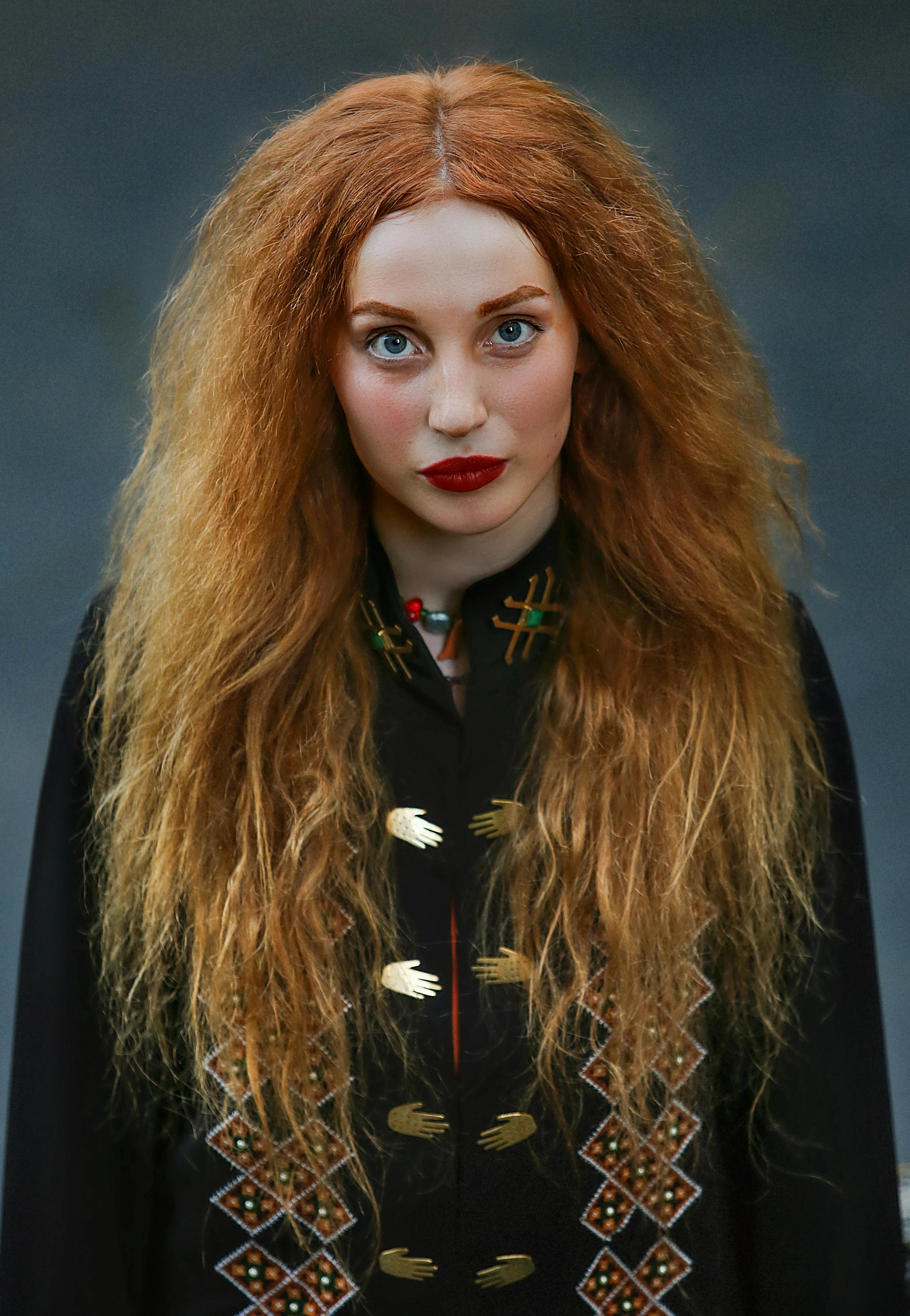 Striking portrait of a woman with flowing red hair, showcasing traditional attire in a captivating, artistic pose.