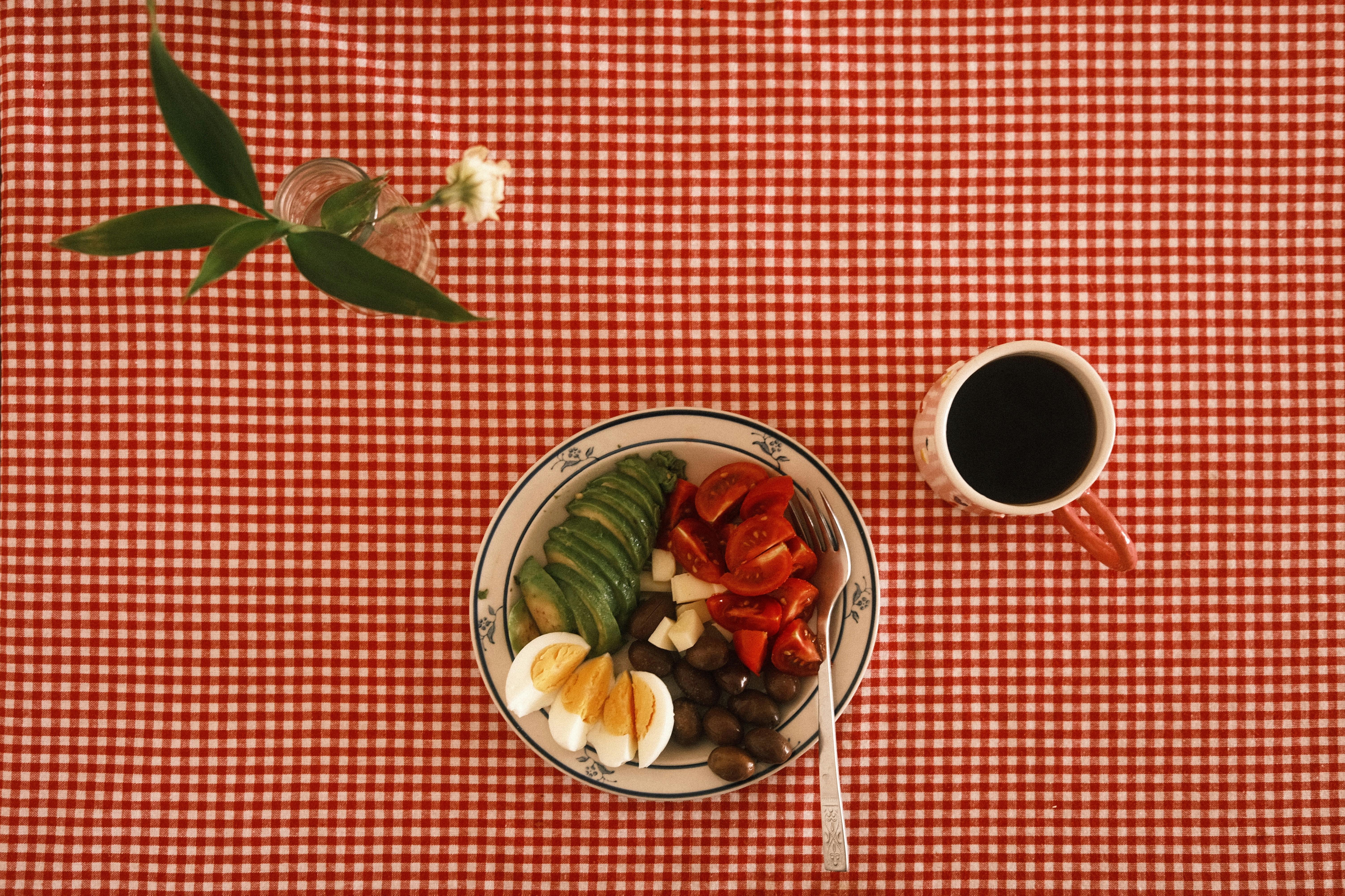 Overhead view of a vibrant breakfast bowl with coffee on a red checkered tablecloth, embodying a cozy, vintage aesthetic.