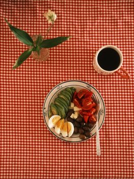Vintage aesthetic breakfast with avocado, eggs, tomatoes, and coffee on a checkered tablecloth.