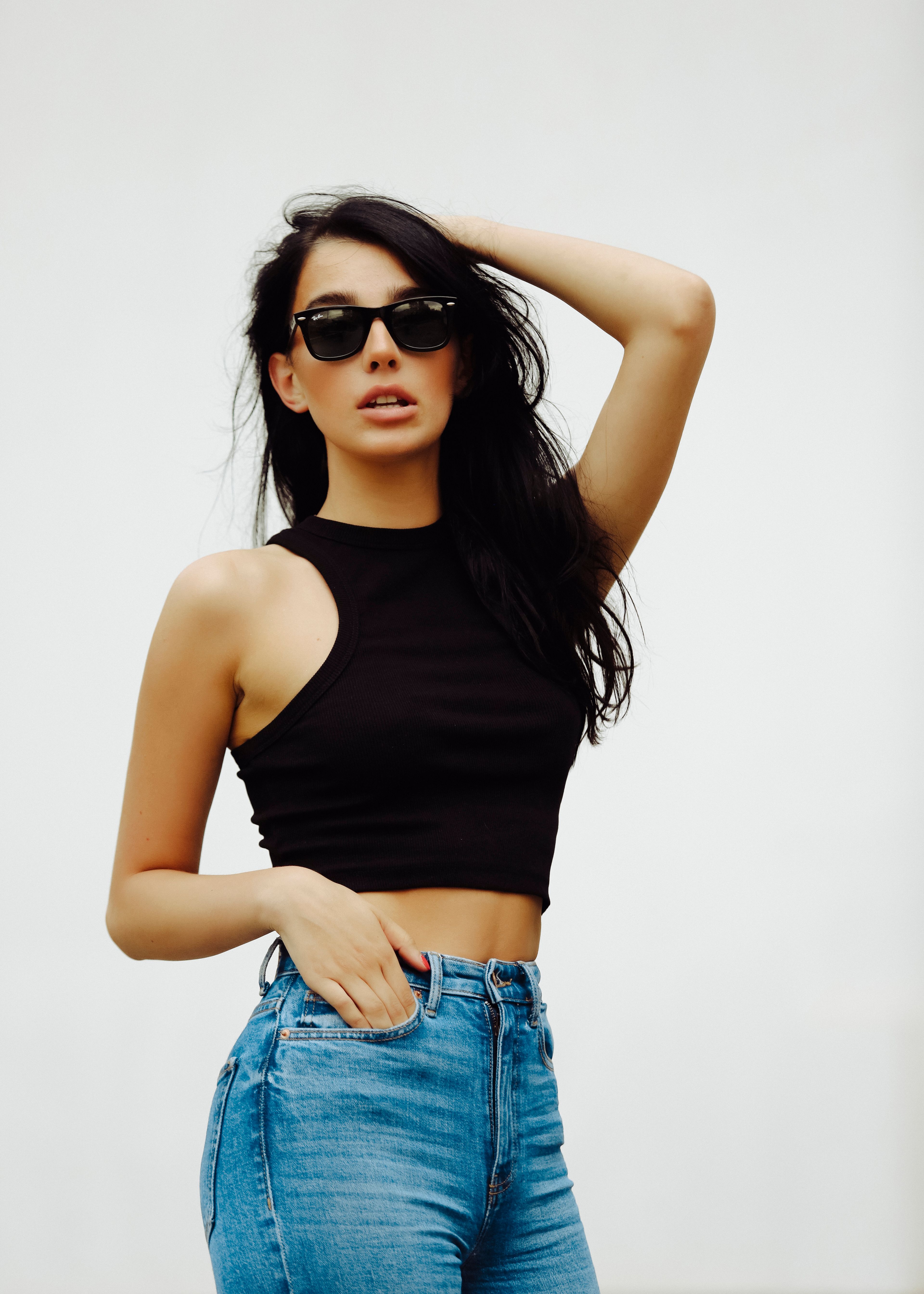 Stylish woman posing confidently in denim and sunglasses against a minimalistic backdrop.