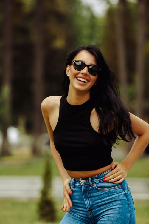 Free Fashionable woman smiling confidently in sunglasses and black top outdoors during the day. Stock Photo