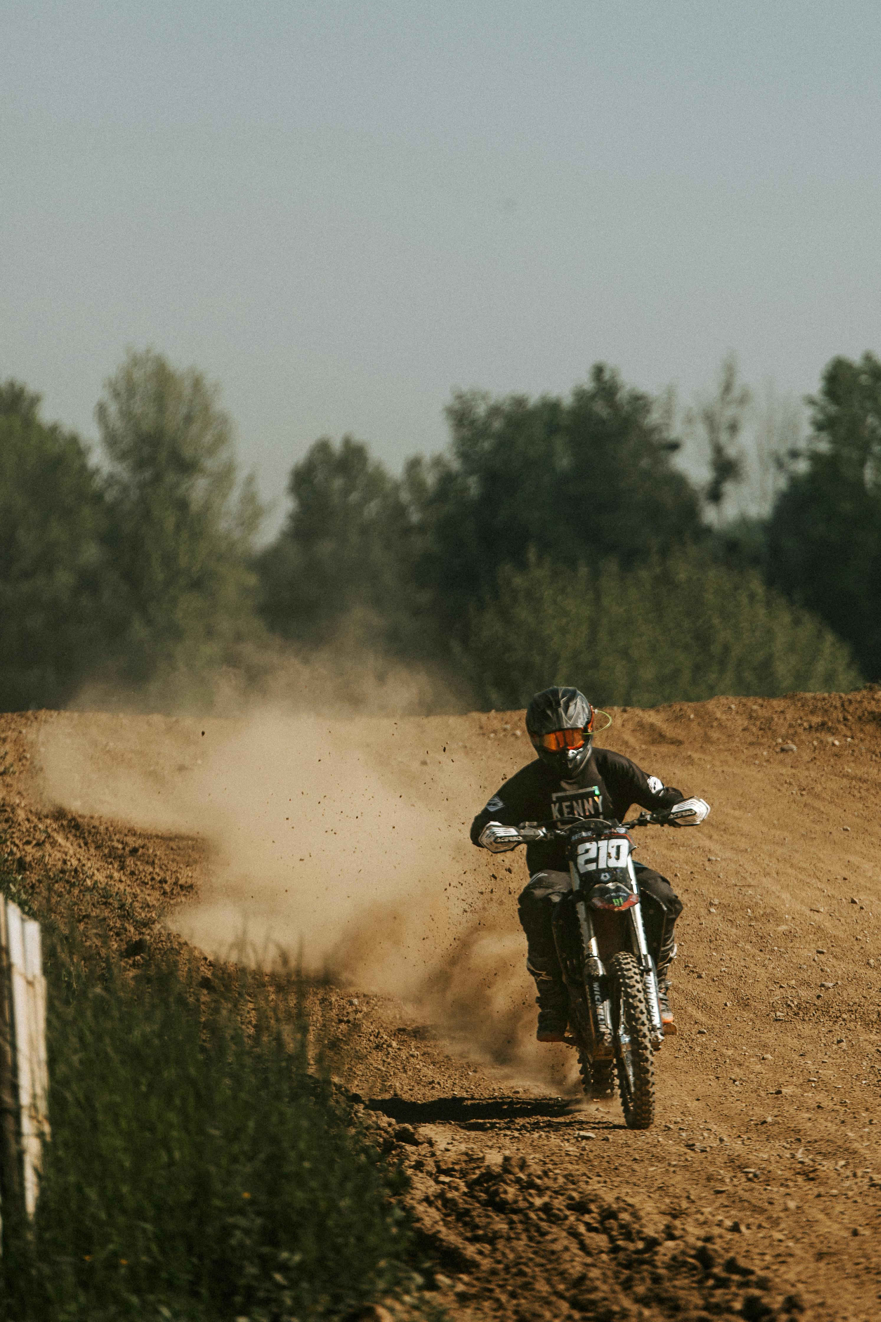 Motocross rider racing on a dirt track, kicking up dust in an outdoor setting.