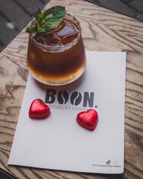 Explore a refreshing espresso tonic with mint, paired with heart-shaped chocolates on a cafe table.